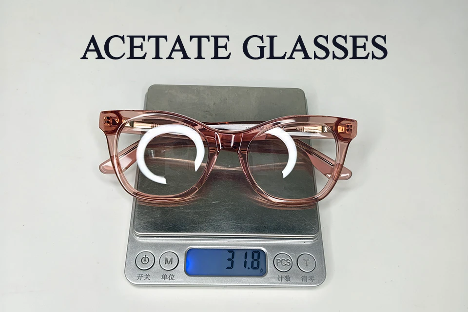 A pair of rose-colored acetate glasses on a digital scale displaying a weight of 31.8 grams, highlighting the material's premium density.