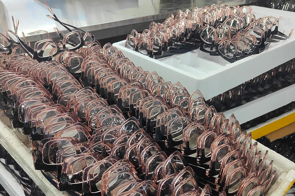 Rows of black and clear pink eyeglasses stacked in white trays.