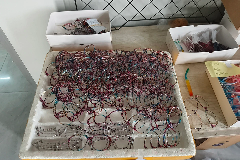 Mass production of colorful acetate eyeglass frames and temples organized in trays at an eyewear factory.