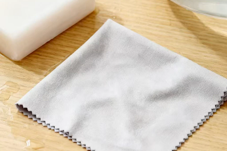 A square grey microfiber cleaning cloth with zigzag decorative edges resting on a light wood surface.