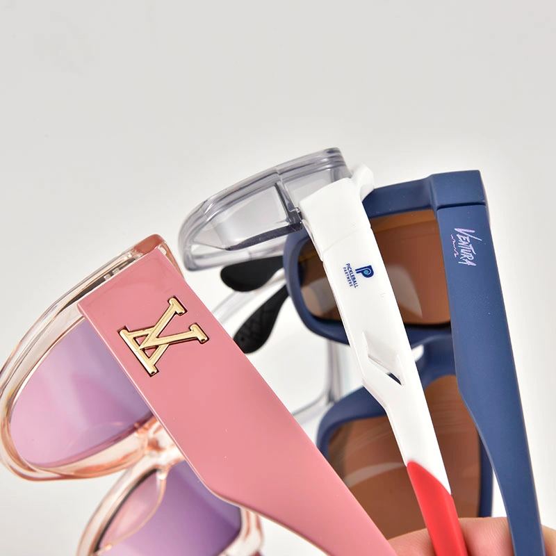 Close-up of custom eyewear branding techniques featuring a gold metal inlay logo on a pink frame and silk-screen printed logos on white and blue temples.